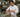 A professional chef in a commercial kitchen places vacuum-sealed meat into a sous vide water bath using an Otiv sous vide machine, which is visible on the counter with its logo displayed clearly.